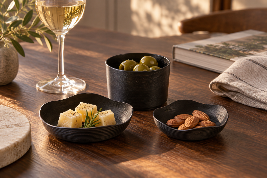 The Sesame set holding olives, cheese, and almonds on a wooden table beside a wine glass and folded cloth.