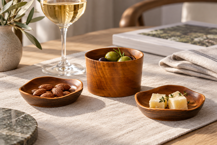 The Mimosa set holding almonds, cheese, and olives on a woven cloth beside a wine glass.