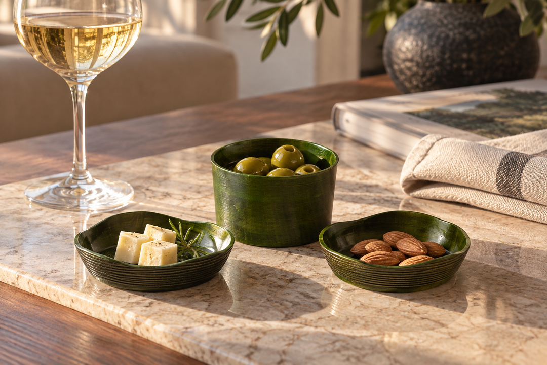 The Olive set holding cheese, almonds, and olives on a pale stone surface beside a wine glass.