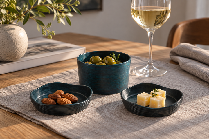 The Hyacinth set holding olives, almonds, and cheese on a gray cloth beside a wine glass.