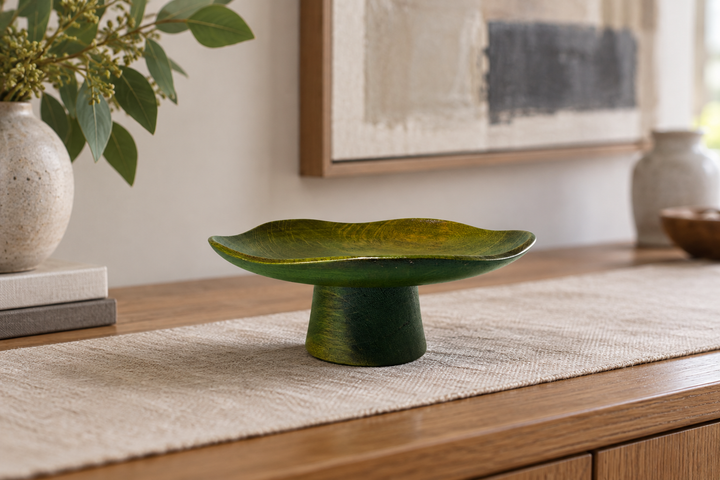 The empty Floating Leaf Olive dish on a neutral runner over a wooden console near books, a vase, and artwork.