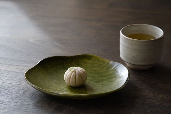 RIN 5.0 Olive plate presenting one small confection beside a tea cup on a calm tabletop.