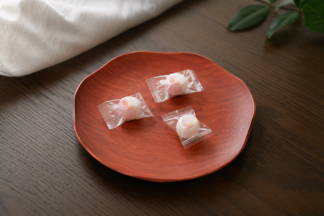 A few individually wrapped sweets arranged sparsely on the berry-red RIN 7.0 lacquerware plate for guests.