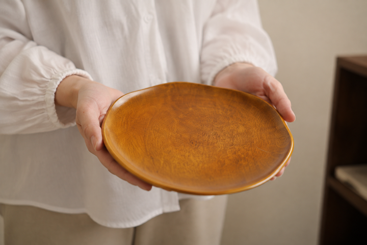Adult hands supporting the empty Mimosa RIN 7.0 lacquerware plate to show its 210-millimeter scale.