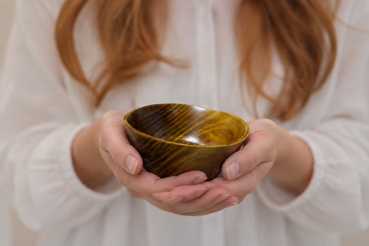 Adult hands gently supporting the empty RIN Bowl S Mimosa close to the body.