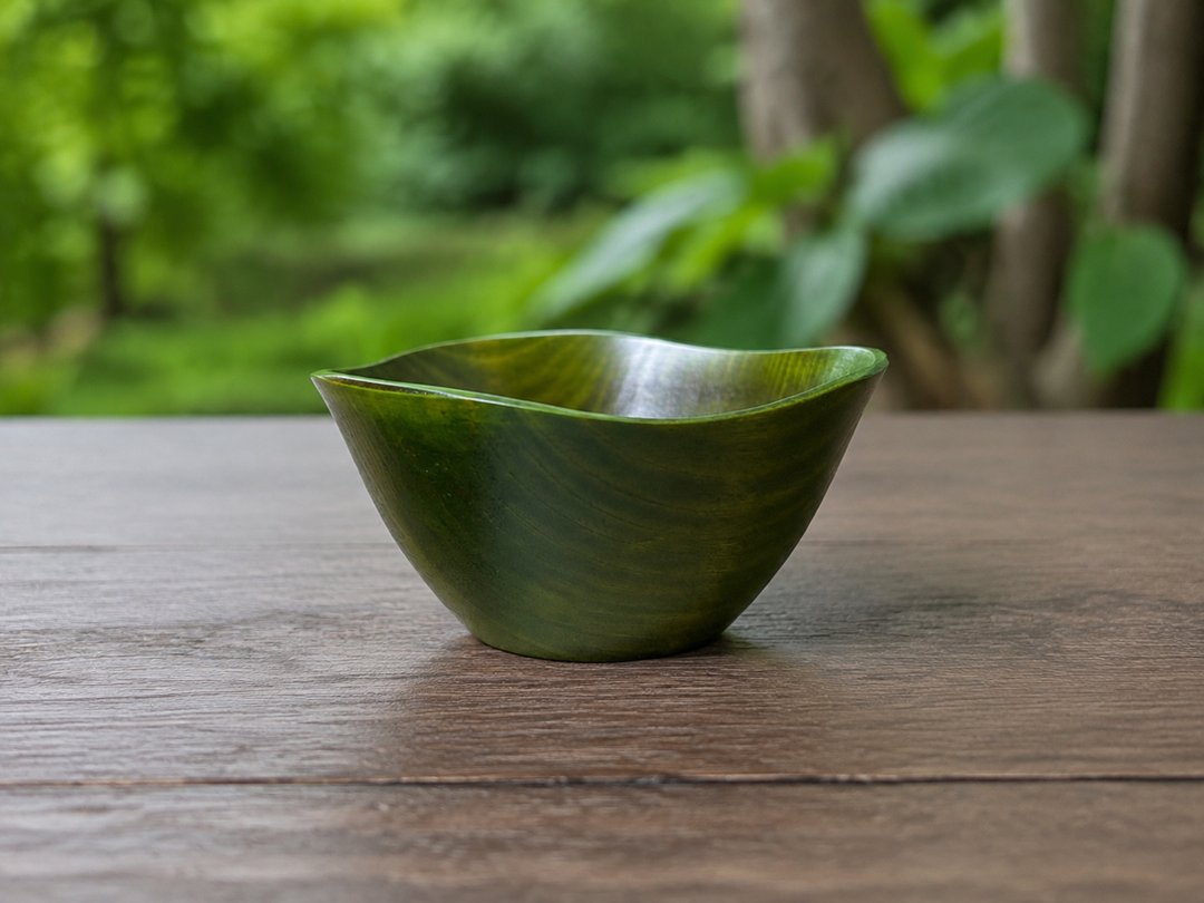 RIN Bowl M Olive resting temporarily on a stable shaded outdoor table with soft greenery in the distance.