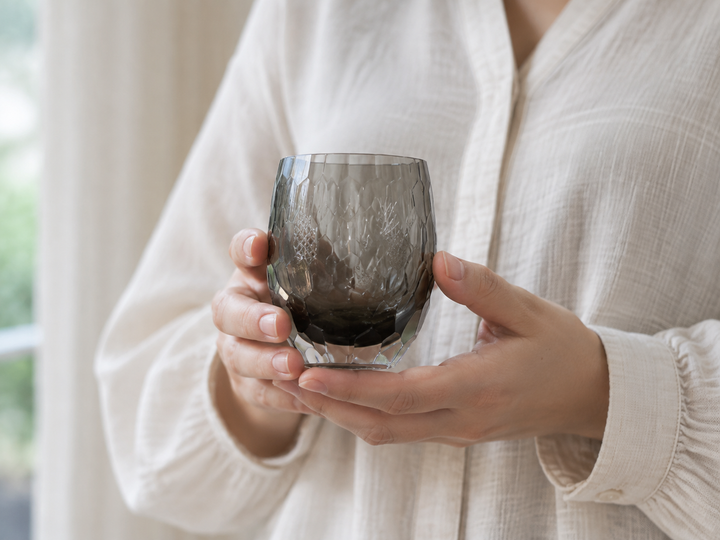 Adult hands securely supporting the empty HYOUSYOU Blue Ink Edo Kiriko glass to show its true scale.