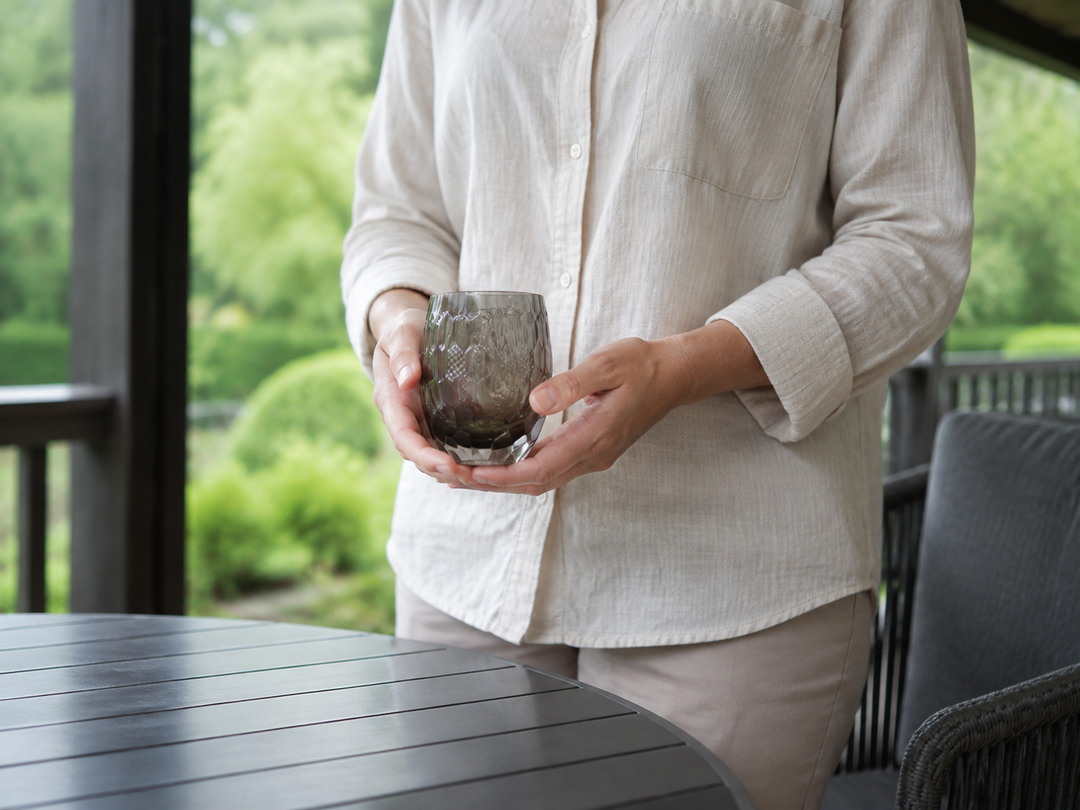 Adult carrying the empty HYOUSYOU Blue Ink Edo Kiriko glass securely toward a shaded outdoor table.