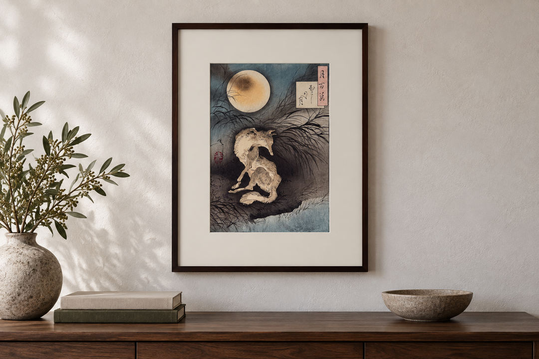 Moon at Musashino Plain displayed above a wooden cabinet with a vase, books, and a shallow bowl against a pale wall.