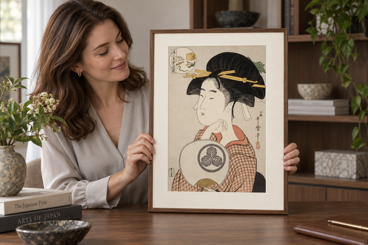A woman looking at the framed Tomimoto Itsutomi print standing upright on a wooden table.