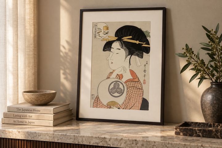 The framed Tomimoto Itsutomi print displayed on a stone console between stacked books and a dark vase.