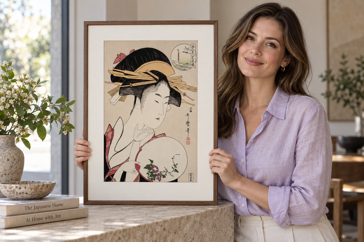 A woman holding the framed Kisegawa of the Matsubaya print upright on a pale stone surface.