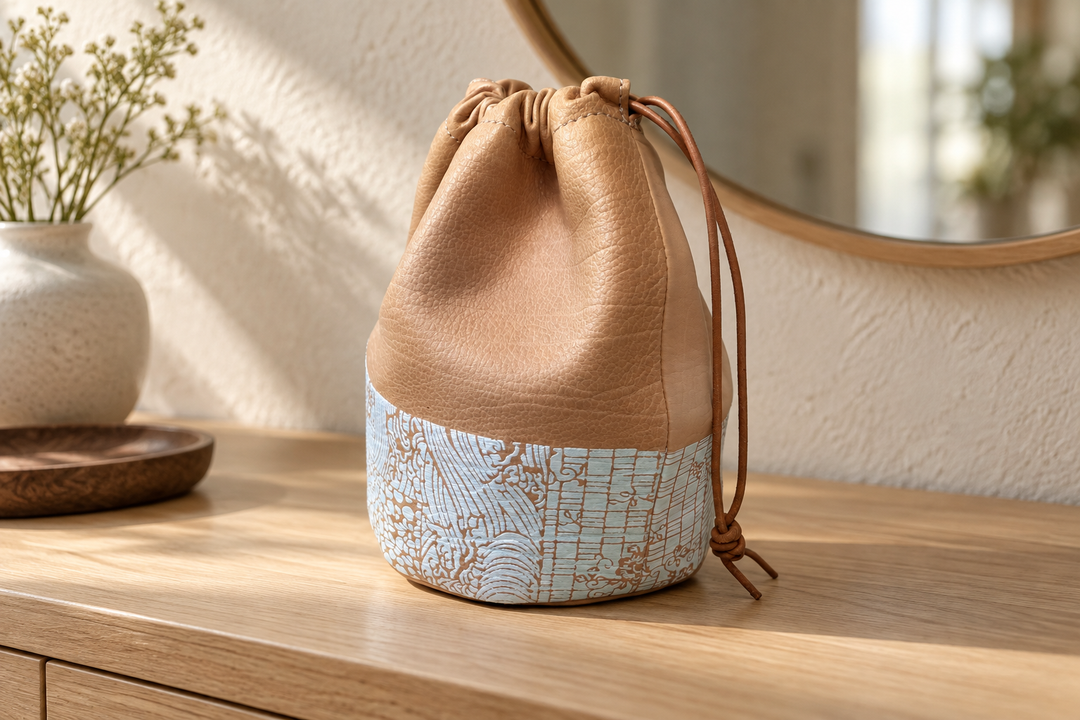 A hand placing a slim card holder into the open natural leather Edo Komon drawstring pouch on an entryway console.