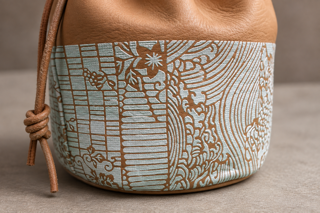 Close view of the pale blue-and-white Edo Komon patterned band, leather grain, seam, and drawstring knot on the natural pouch.