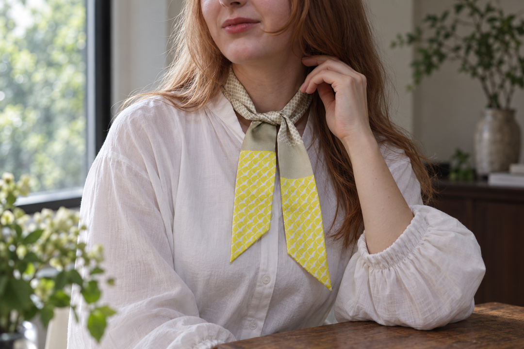 A narrow yellow and grey-green silk scarf tied once at the neck over a plain white blouse.