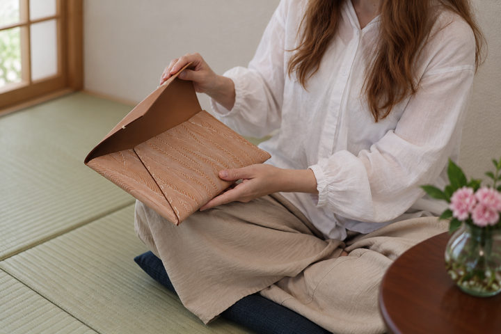 The natural leather Edo Komon clutch opened carefully across the lap in a quiet tatami room.