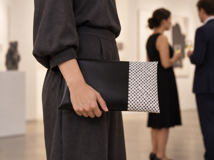 A person in a restrained dark outfit holding the black-and-white Tokyo Some-Komon clutch at an indoor gallery reception.