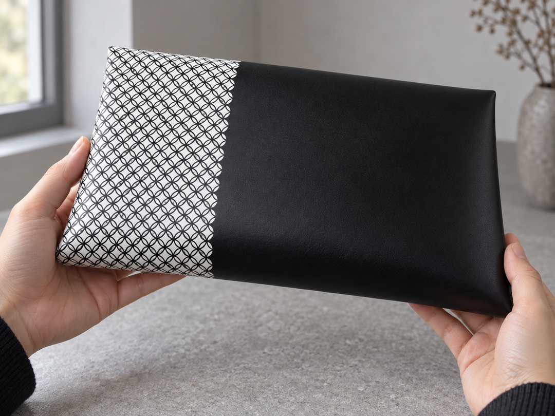 A close three-quarter view of the clutch being turned by hand, showing the fine black repeat wrapping around the white panel into smooth black leather.