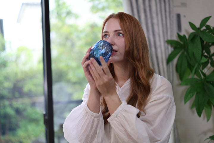 Woman holding the indigo Edo Kiriko glass with both hands near a bright window