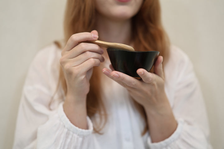 Adult model supporting the empty RIN Bowl S Sesame while holding a wooden spoon above its irregular rim.