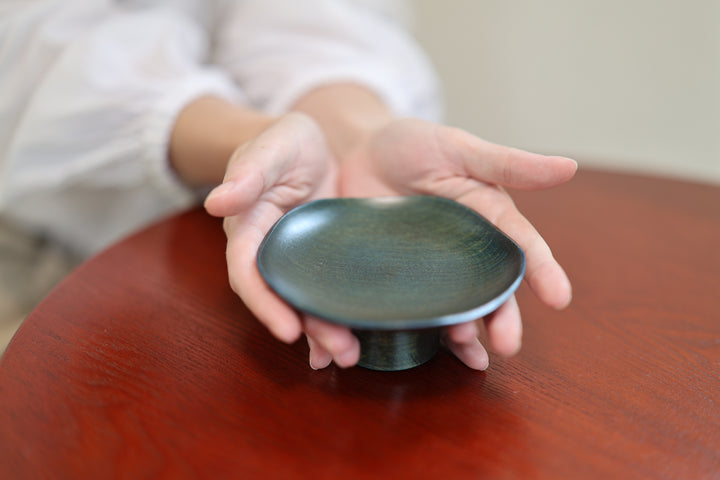 Cradled in both hands, the Floating Leaf reveals its compact scale and elevated construction. The photograph shows the exact supplied product, including its softly irregular blue-green upper surface and darker pedestal.