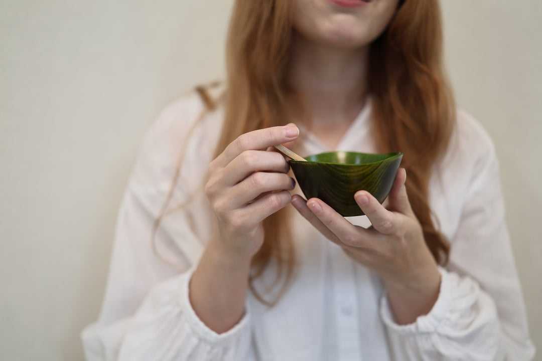 Adult model holding the empty RIN Bowl S Olive close to the camera with a wooden spoon at the rim.