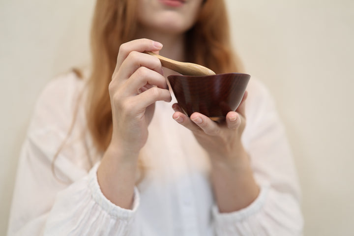 Adult model holding the RIN Bowl S Lilac close to the camera with a wooden spoon above the bowl.
