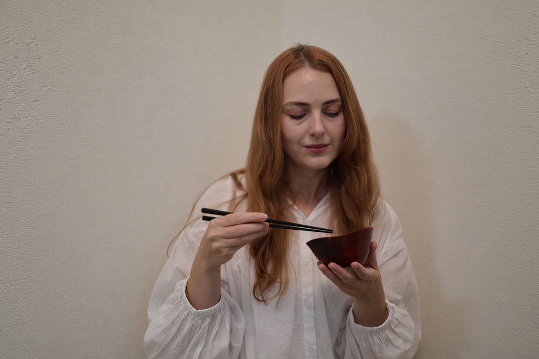 Adult model holding the empty RIN Bowl M Berry with chopsticks above its softly rising rim.
