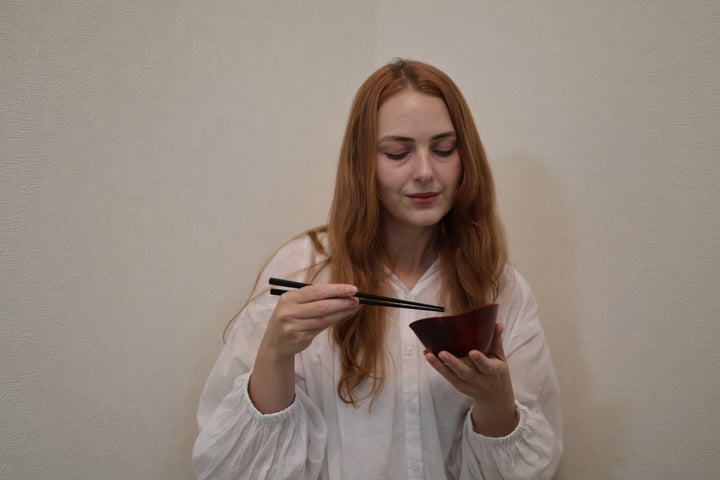 Adult model holding the empty RIN Bowl M Berry with chopsticks above its softly rising rim.