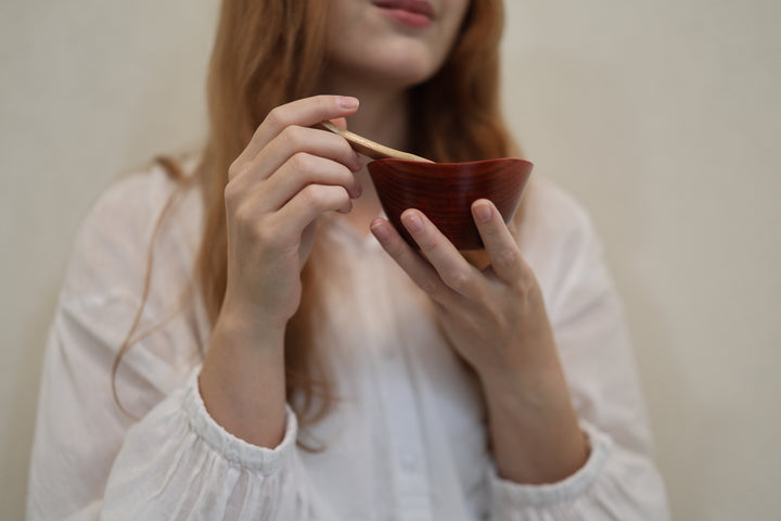 An adult model holding the empty RIN Bowl S Berry close in both hands indoors.