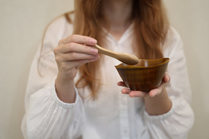 Adult model holding the empty RIN Bowl M Mimosa close to the camera with a wooden spoon above its irregular rim.