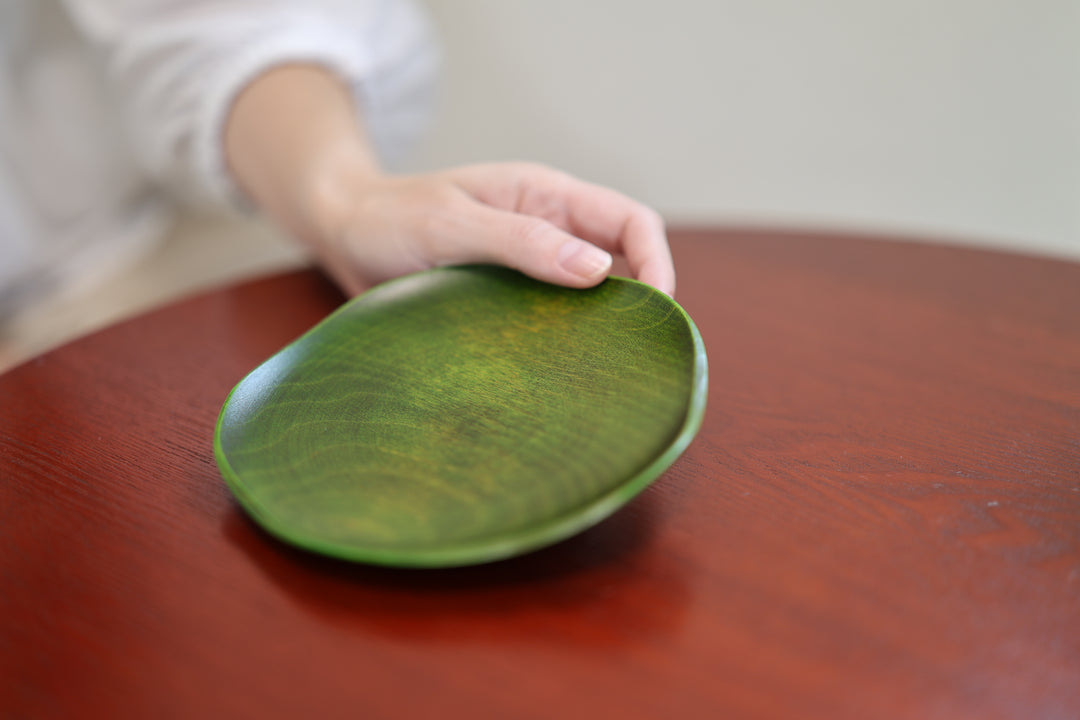 A hand resting lightly on the rim of the RIN 5.0 Olive plate on a red-brown table.