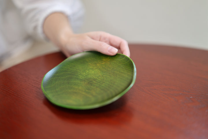 A hand resting lightly on the rim of the RIN 5.0 Olive plate on a red-brown table.