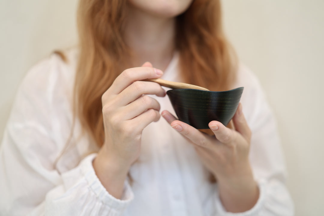 Adult model holding the RIN Bowl S Hyacinth close to the camera with a wooden spoon above the bowl.