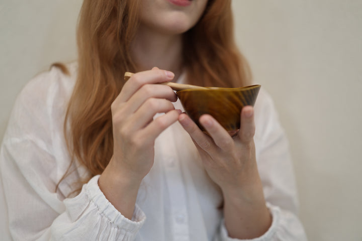 Adult model holding the RIN Bowl S Mimosa close to the camera with a wooden spoon above the empty bowl.