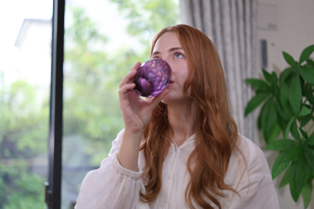 A person drinking from the purple Edo Kiriko glass beside a bright window.