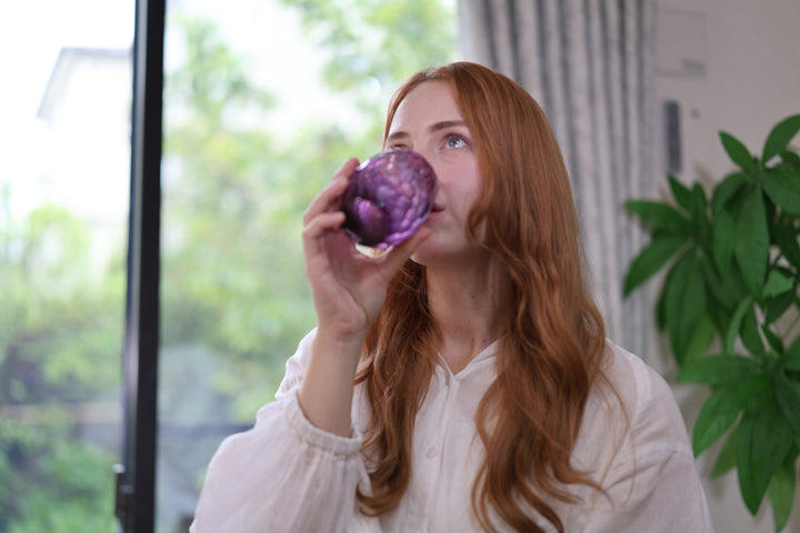 A person drinking from the purple Edo Kiriko glass beside a bright window.