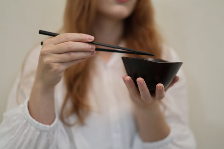 Adult model holding the empty RIN Bowl M Lilac with chopsticks above its undulating rim.