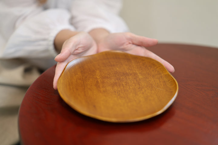 Adult model presenting the empty RIN 7.0 Mimosa plate with open hands on a low table.