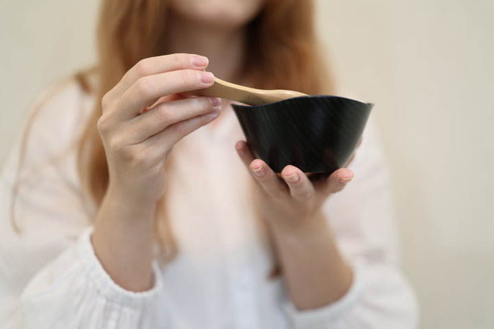 Adult model supporting the empty RIN Bowl M Hyacinth while holding a wooden spoon above its irregular rim.