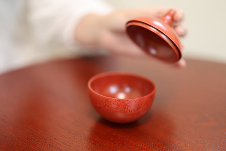 A hand lifting the lid from the red Bulb: Berry on a wooden table