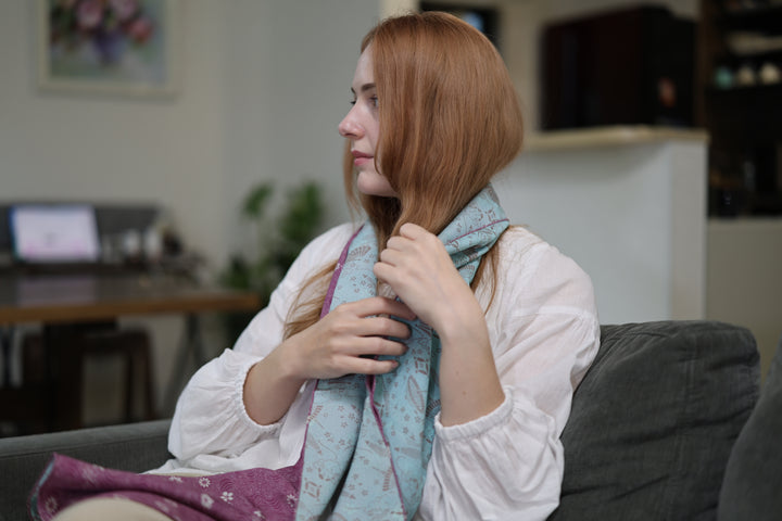 A seated wearer draped in the blue and purple double-sided silk stole in a living room.