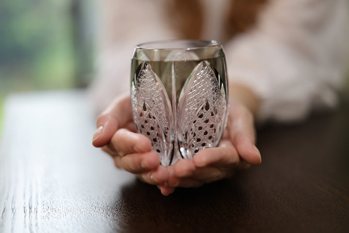 The Korohana Edo Kiriko vessel cradled in two hands above a dark table.
