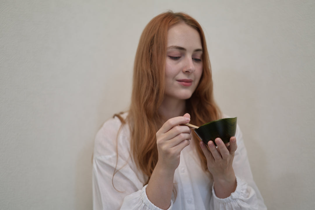 Adult model holding the empty RIN Bowl S Olive at chest height with a wooden spoon beside its raised rim.