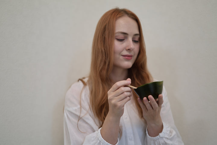Adult model holding the empty RIN Bowl S Olive at chest height with a wooden spoon beside its raised rim.
