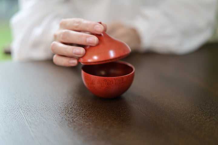 A hand lifting the lid from the red Bulb: Berry on a dark table
