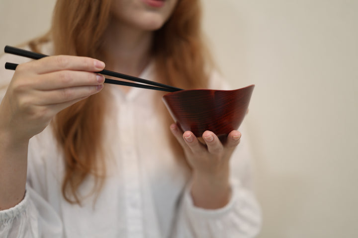 Close view of an adult model supporting the empty RIN Bowl M Berry while holding chopsticks above it.
