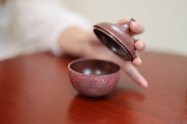 The open lilac lid beside the rounded wooden body on a table