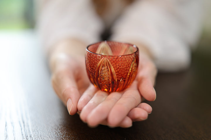 GENEN Gold-Red and Amber Edo Kiriko glass resting on the open palm of an adult model.