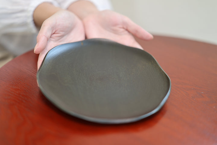 A hand approaching the low rim of the RIN 7.0 Sesame on a red table.